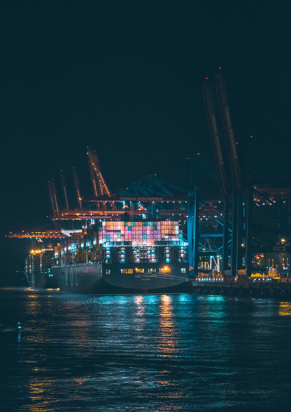 A large container ship being unloaded by cranes at night.