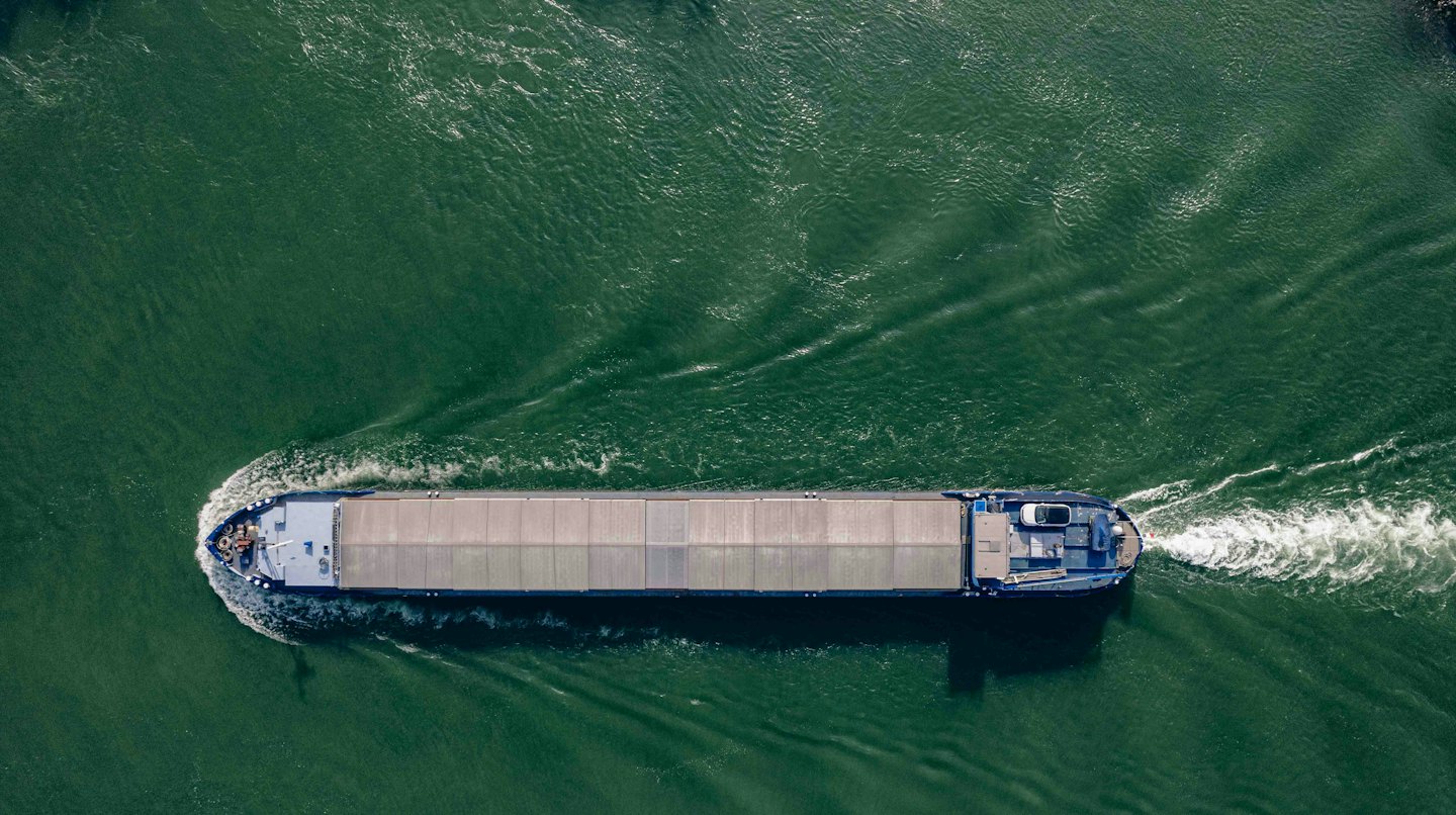 A dark blue cargo barge travels across deep green water.