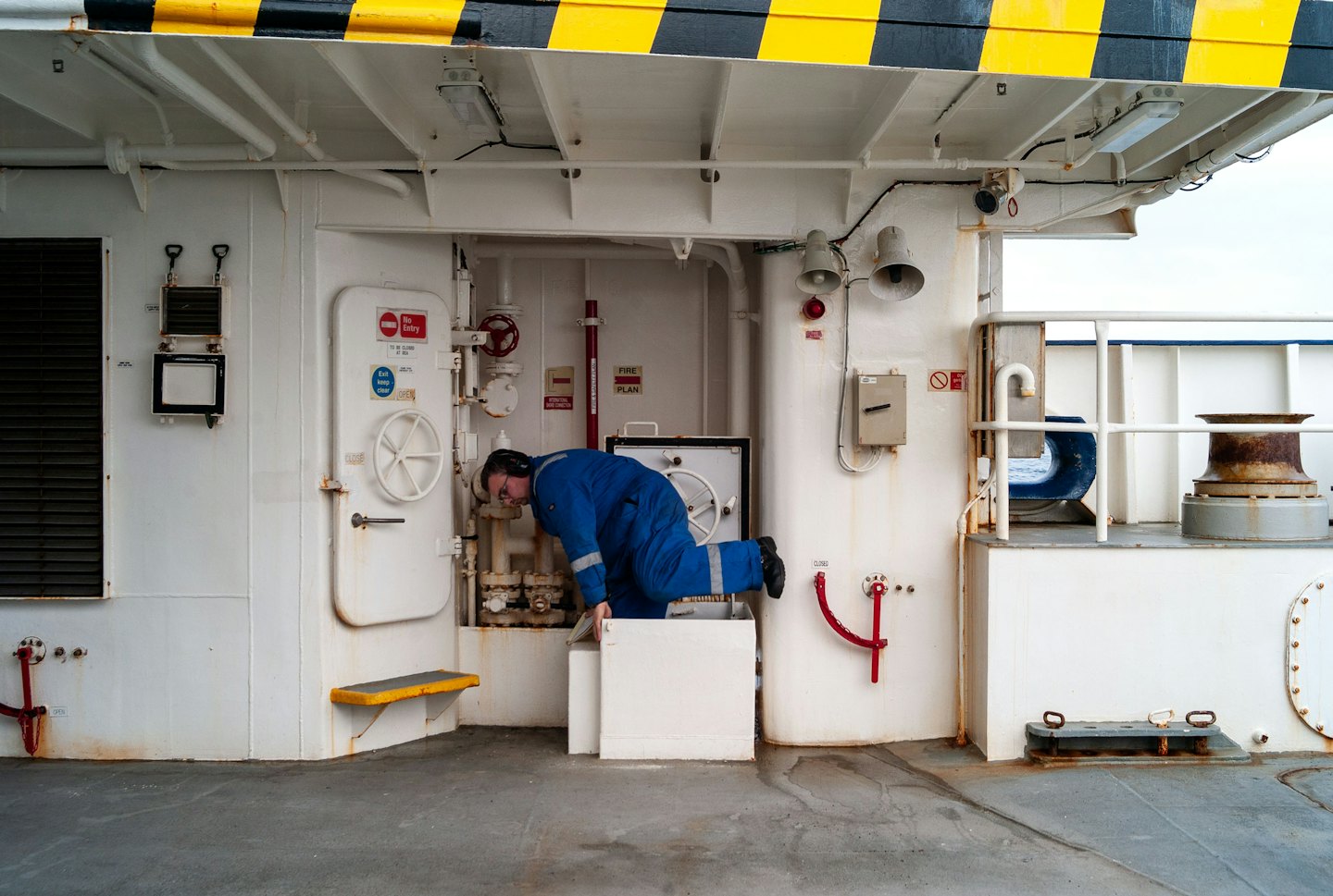 Technician in blue overalls inspects machinery on an industrial deck.